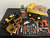 Full lot of over 40 construction-themed toy tools and vehicles laid out on black table.