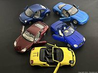 Five assorted die cast cars arranged on black surface with all doors open to show detail and condition.