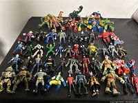 Overhead view of all action figures laid out on black surface showing various superheroes and villains including Batman, TMNT, Iron Man, Spider-Man.