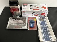 Five kitchen items together on black surface: OXO Mandoline Slicer box, KitchenAid coffee filters box, tablecloth protector, blue kitchen towel, small blue tank flapper in packaging