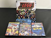 Full lot view showing LEGO minifigures arranged on baseplates, LEGO Billund Denmark metal sign behind, and three DVDs in front.