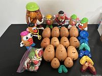 Overview shot showing multiple Mr. Potato Head bodies, figures with hats, and a bag of assorted parts, arranged on a black surface.