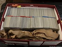 Large quantity of Pokémon cards tightly packed inside a brown snack box, separated with colored dividers, showing card edges and condition.