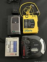 Photo showing four audio players from Sony and Toshiba: a black Sony cassette-corder TCM-85V, a yellow Sony Walkman Sports WM-F73, a silver Toshiba KT-V31 cassette player, and a Sony Discman D-555 CD player with wired earphones.