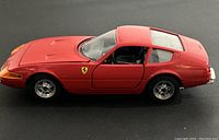 Red die cast Ferrari 365GTB/4 Daytona model car photographed from side showing detailed profile including wheels, Ferrari emblem, and door outlines.