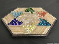 Top view of hexagonal marble Chinese checkers board with blue, green, orange, dark blue, yellow, and turquoise marbles arranged in triangular sets.