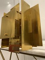 Angle showing overlapping brass plates and structural knobs, highlighting the abstract modern design.