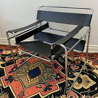 Three-quarter front view showing tubular chrome steel frame and black leather strap seat, arms and back