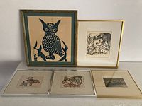 Full view of five framed prints arranged in two rows showing owl, portrait etching, indigenous designs, landscape