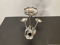 Front angle of silver plated antique epergne showing central and side trumpet branches with ruffled edges on round base.