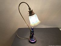 Full view of antique lamp showing iridescent glass base and brass arm holding swirled frosted glass shade