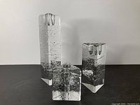 Front view of three glass candle holders with internal bubble patterns on a black surface against white wall