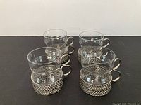 Front angle showing all four glasses with silver woven metal holders and looped handles arranged in a row