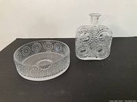 Photo showing the large round glass bowl and rectangular decanter with textured bubble motifs on a table.