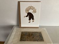 Top view of two Inuit art prints stacked, one featuring a figure with multiple animal heads arranged in an arc, unframed and signed.