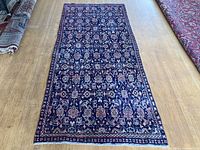 Full view of a vintage Mahal Persian runner hand knotted wool rug with navy blue base and pink, cream floral and geometric border pattern laid on a wooden floor.