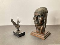 Photo showing bronze swan sculpture on black stone base along with Peruvian wood bust sculpture