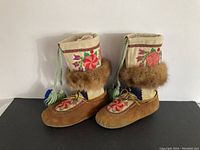 Pair of womens vintage muckluks shown from side view on black surface with clear details of suede, fabric, embroidery, and fur trim.