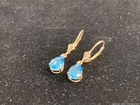 Front oblique view of pear-shaped blue topaz earrings set in 14KT gold on black background