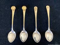 Four sterling silver teaspoons displayed on a dark fabric background, showing engraved names inside spoons and gold nugget embellishments on handles.