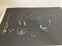 Overview of seven necklaces arranged on a flat black surface, showcasing variety in style and materials.