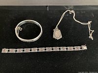 Overview of three pieces: hinged bangle bracelet, linked bracelet with red gemstones, and pendant on chain