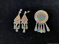 Full view of the set showing pair of earrings and pendant/brooch on black background