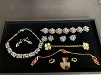 All nine items arranged on black tray showing necklaces, bracelets, earrings, and brooch