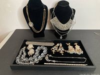 Overall photo of jewelry displayed on black velvet tray and black busts including necklaces, bracelets and earrings.