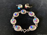 Photo of bracelet and one earring showing colorful inlays and sterling silver scalloped edges