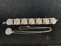 Photo showing full bracelet with seven coin measures and matching pendant on chain against black background