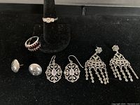 Photo shows the full set of three pairs of silver earrings and two rings on black display.