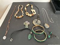 Photo showing multiple stone jewelry items including necklaces, bracelets, pendants, and earrings arranged on a white surface.