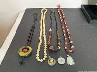 Overview of five bead necklaces and three jade pendants laid out on black surface
