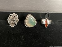 Overall photo showing three silver rings with different stones and designs on a black surface.