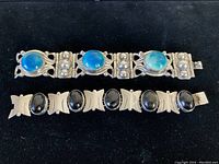 Both bracelets laid flat, showing the full length and design. One bracelet has round blue-green turquoise stones with ornate silverwork, the other has smooth oval black onyx stones with bow-shaped silver links.