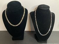 Two chain necklaces displayed on black bust stands, showing overall styles