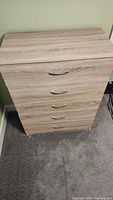 Front view of a 5 drawer dresser showing the wood grain finish and silver handles