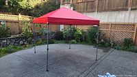 Red pop-up canopy fully set up on patio with red fabric top and metal frame.