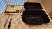 Black enamel steel roaster pan with metal roasting rack, rectangular shape with side handles.
