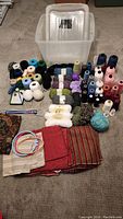 Overview of assorted yarn, thread spools, upholstery fabric, embroidery hoops, crochet hooks, and plastic tote container