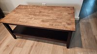 Side angled view of the coffee table showing wood grain top and black legs with lower shelf