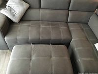 Front corner view of grey microfiber sectional and ottoman with white stitching