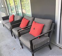 Three dark grey resin wicker seating pieces (sofa and two chairs) on balcony with grey cushions and red pillows