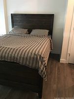 Assembled king bed with dark wood frame, headboard, mattress and striped sheets