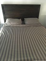Dark wood headboard and frame with striped sheets and two pillows