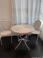 Photo of the bistro set showing the white metal table with wicker top and two matching chairs with wicker seats and decorative metal backs.