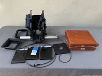 Full lot overview showing Toyo 4x5 studio camera on rail with bellows, three 4x5 film holders, dark cloth, and brown leather carrying case for Polaroid camera.