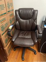 Front angled view of brown leather office chair showing padded seat, backrest, armrests, and caster wheels on floor.