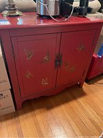 Red wooden cabinet showing butterfly artwork on front doors with ornate metal handles. Shows wear and tear.